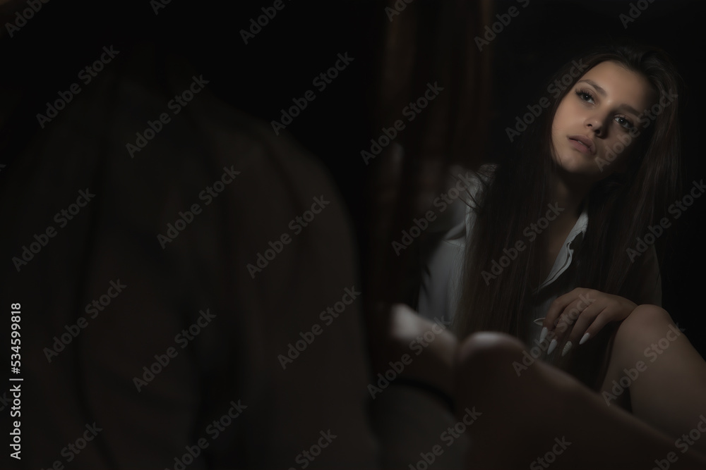 Low key portrait of sitting young woman is looking at her reflection in the mirror. Horizontally. Low key portrait of sitting young woman is looking at her reflection in the mirror. Horizontally.