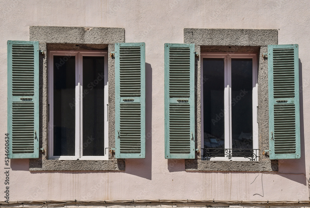 A pair of windows with pale green shutters and stone frames, France