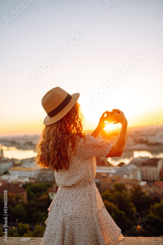 Young Woman on vacation using mobile phone to take photo of the sunset of the city. Rest, relaxation, lifestyle concept.