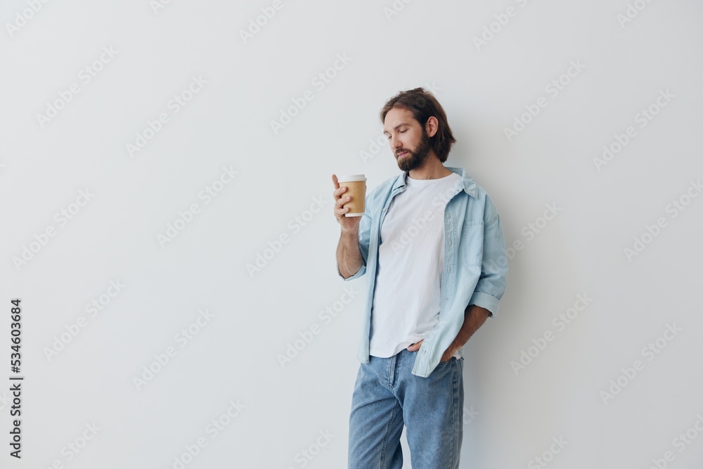 Freelance Millennial man with a beard drinking coffee from a recycled cup in stylish hipster clothes white T-shirt blue jeans and shirt on a white background Freelance Millennial man with a beard drinking coffee from a recycled cup in stylish hipster clothes white T-shirt blue jeans and shirt on a white background