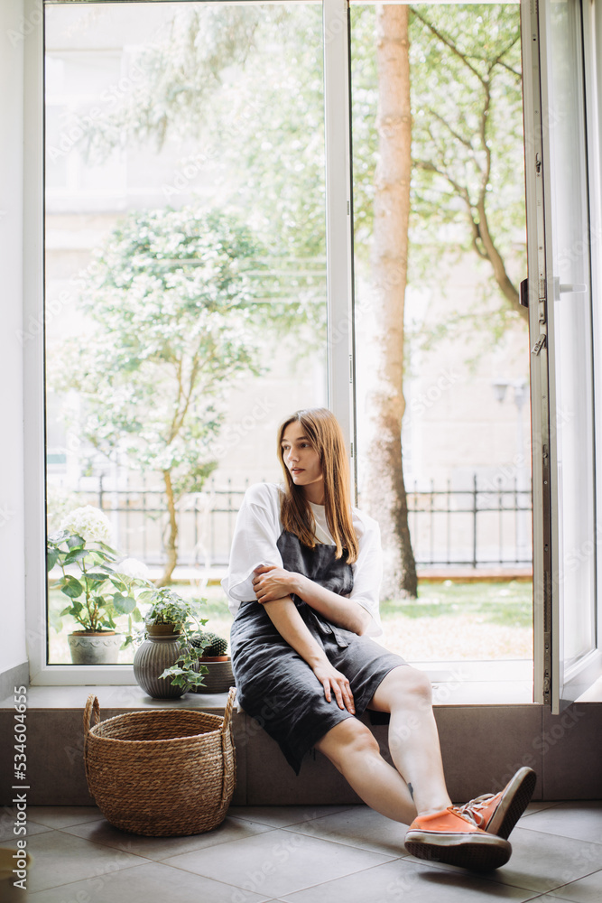 A young woman sits by the window in her flower shop. Small business concept. A young woman sits by the window in her flower shop. Small business concept.
