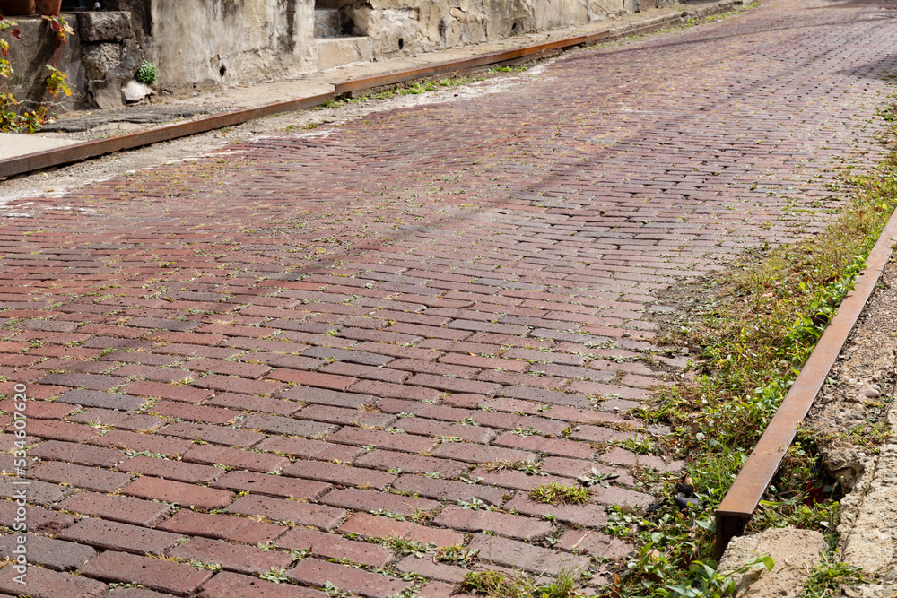 Bright sunlight reflecting off a red brick street with rusted metal ...