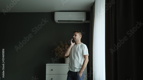 Man in home clothes calls on mobile phone in room with air conditioner. photo