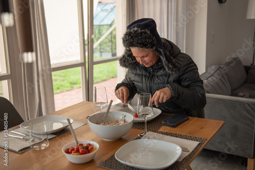 A woman sits at the dining table, dressed warmly, and eats