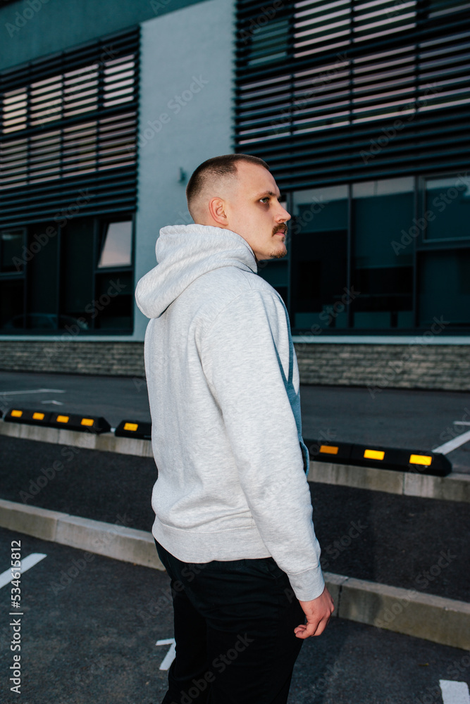 City portrait of handsome guy with mustache and beard wearing gray blank hoodie with space for your logo or design. Mockup for print