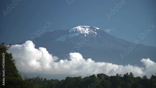 Long time lapse of white clouds move below majestic Kilimanjaro snowy mountain... photo
