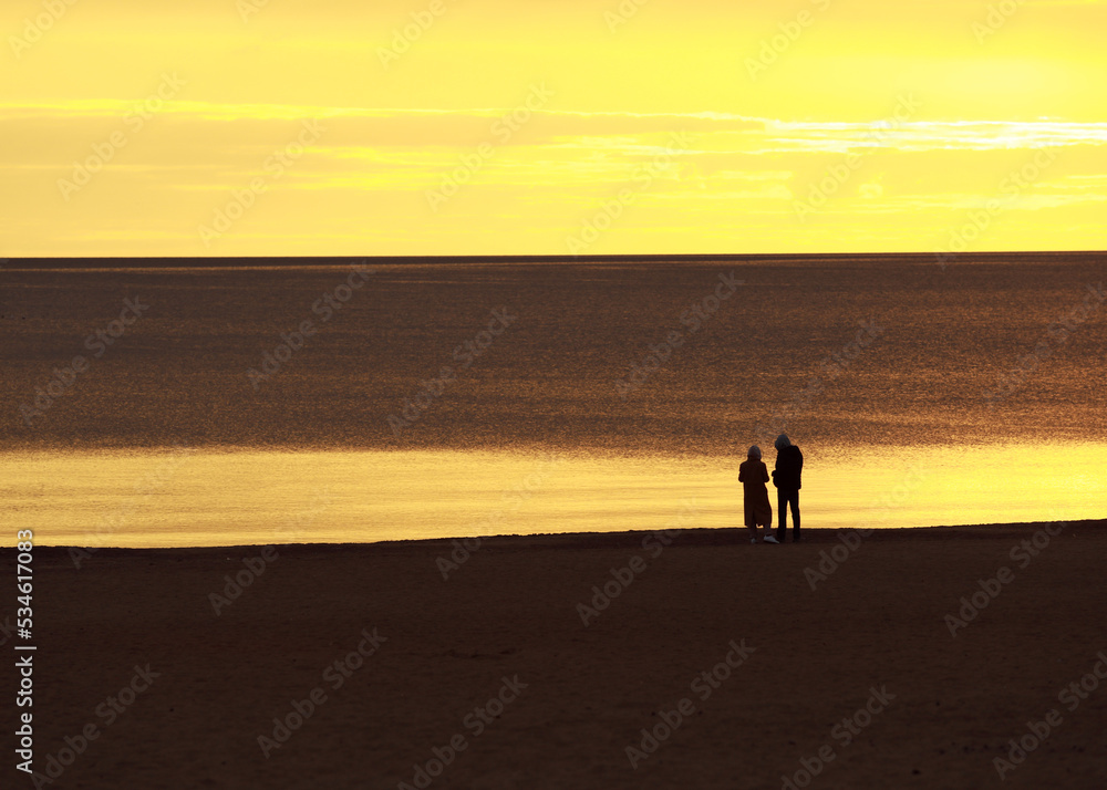 a young couple on the shore looks towards the sunset, a beautiful romantic sunset photo a young couple on the shore looks towards the sunset, a beautiful romantic sunset photo