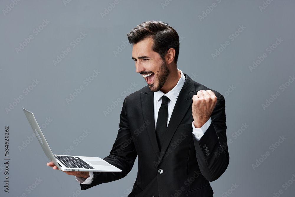 Man business looks into laptop and works online via internet in business suit video call happy smile with teeth fist bump on gray background copy place Man business looks into laptop and works online via internet in business suit video call happy smile with teeth fist bump on gray background copy place