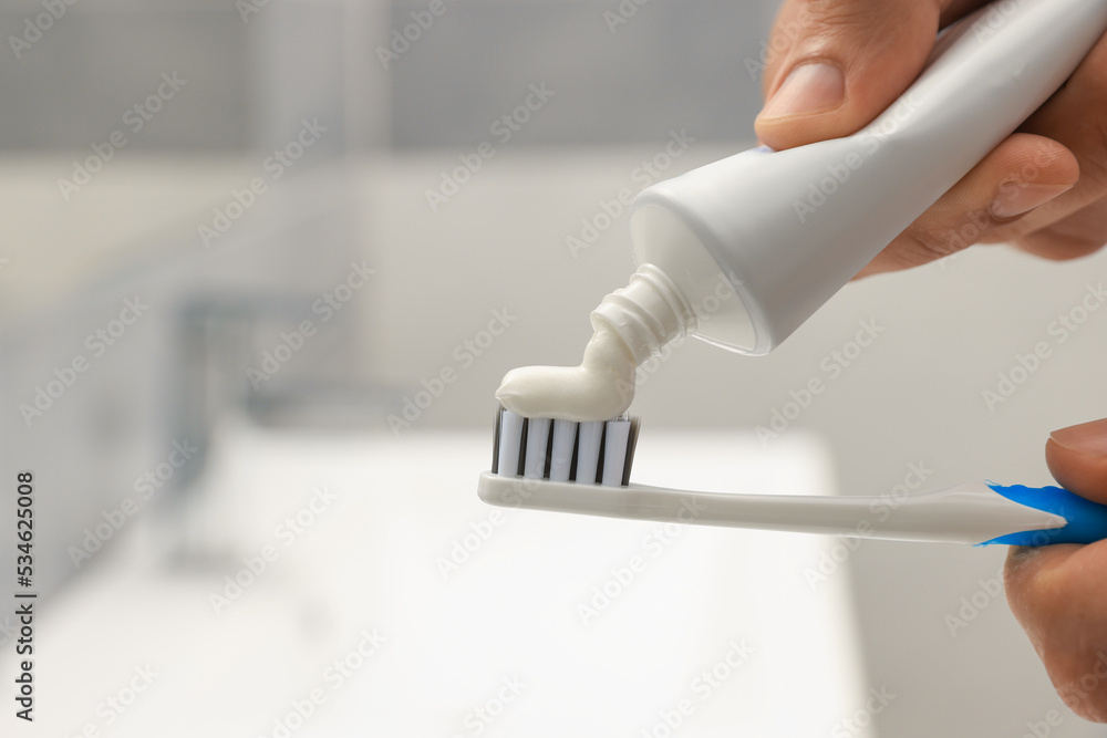 Man applying toothpaste on brush in bathroom, closeup. Space for text