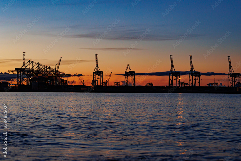 Panoramic image of the cargo port at sunset. Gdansk at night with container terminals, cargo cranes at sea and clear blue sky. Cargo sea port