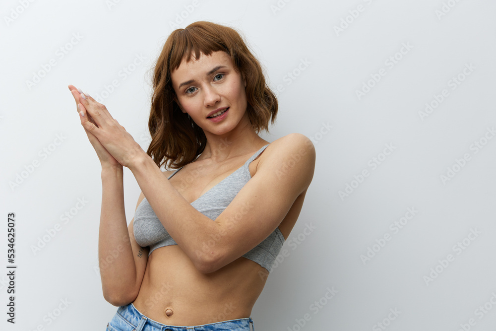 Obraz premium a beautiful, sexy, woman with tanned skin color and red hair, a toned body, stands on a white background holding her hands in a gentle gesture and smiles pleasantly