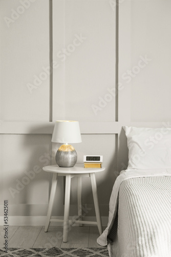 Stylish lamp, alarm clock and book on bedside table indoors. Bedroom interior elements