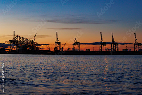 Panoramic image of the cargo port at sunset. Gdansk at night with container terminals, cargo cranes at sea and clear blue sky. Cargo sea port © YURII MASLAK