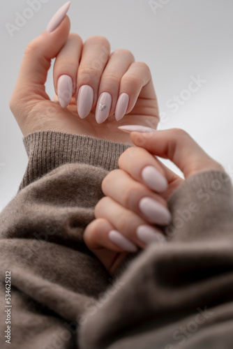 Female hands holding a soft cozy wool sweater blanket - modern pink nails with glitter heart polish design - slim manicured fingers