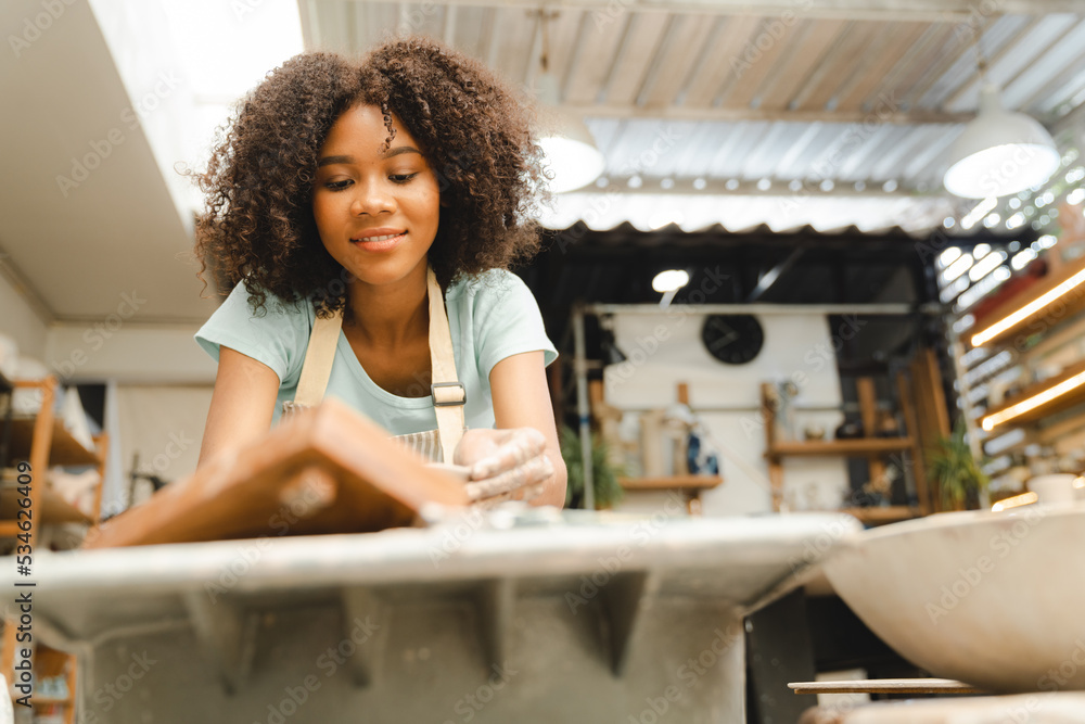 Creative afro American young woman artist molding clay on pottery wheel, Workshop in ceramic studio, clay making of a ceramic pot on the pottery wheel, hobby and leisure with pleasure concept Creative afro American young woman artist molding clay on pottery wheel, Workshop in ceramic studio, clay making of a ceramic pot on the pottery wheel, hobby and leisure with pleasure concept