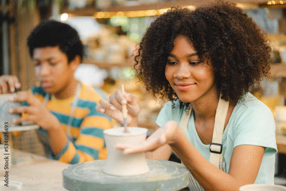 Creative afro American young woman artist molding clay on pottery wheel, Workshop in ceramic studio, clay making of a ceramic pot on the pottery wheel, hobby and leisure with pleasure concept Creative afro American young woman artist molding clay on pottery wheel, Workshop in ceramic studio, clay making of a ceramic pot on the pottery wheel, hobby and leisure with pleasure concept