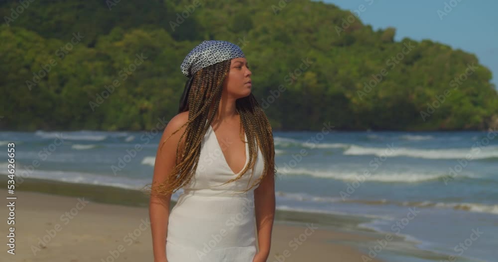 Young girl in a beach dress walking on the golden sands of a tropical beach with waves of the ocean crashing in the background Young girl in a beach dress walking on the golden sands of a tropical beach with waves of the ocean crashing in the background
