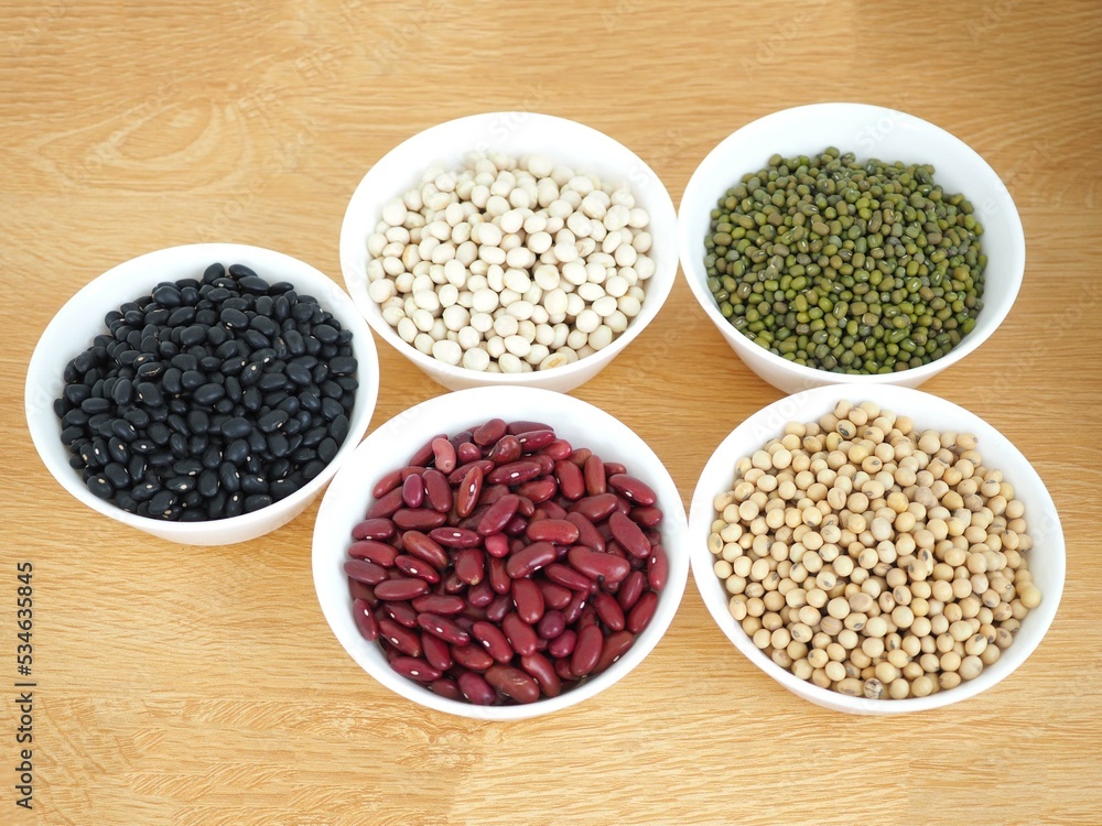 Natural grains consisted of black beans, green beans, red beans, soybeans and white beans in cup on wooden background.