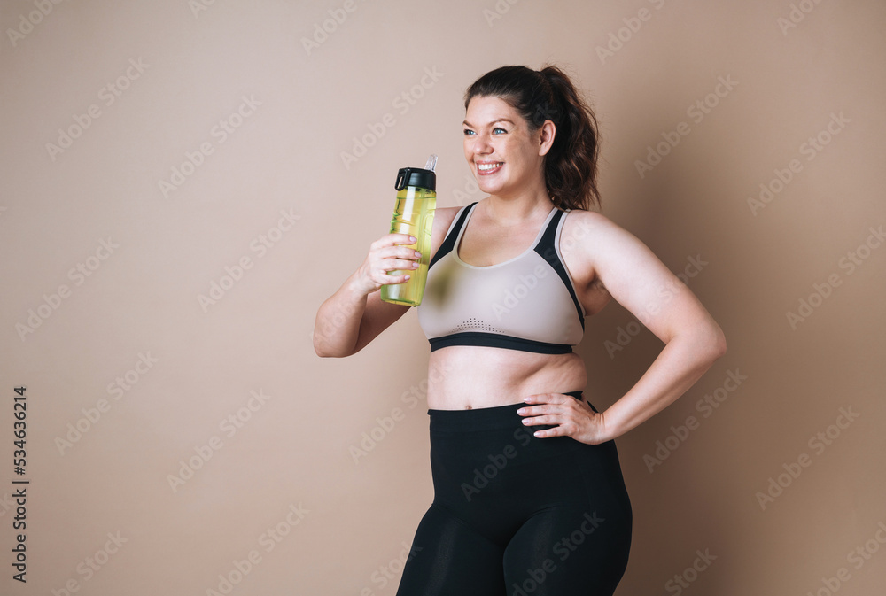 Self loving young woman plus size in sport with bottle of water on beige background, body love Self loving young woman plus size in sport with bottle of water on beige background, body love