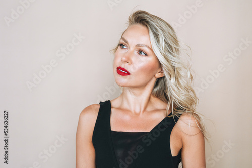 Portrait of gorgeous happy blonde young woman with bright makeup in evening dress on beige background