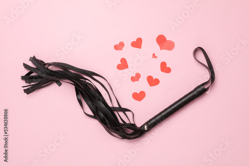 Leather whip from sex shop with hearts on pink background. Sex, love games