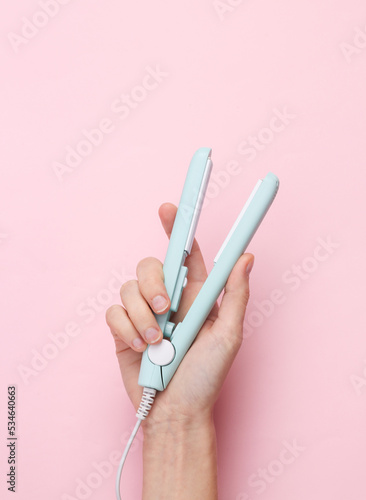 Mini hair straightener in a female hand on a pink background
