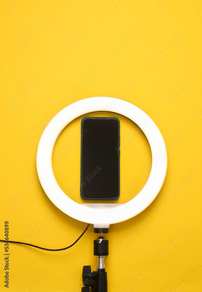 Led ring lamp with smartphone on yellow background. Gear for blogging