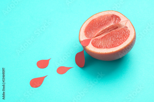 Menstruation concept  women s health. Ripe grapefruit half vagina symbol with blood drops on blue background. creative idea