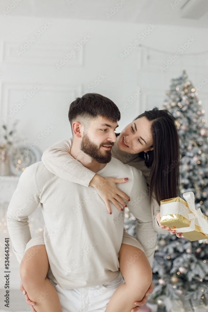 Man holding a woman piggyback near Christmas tree Man holding a woman piggyback near Christmas tree