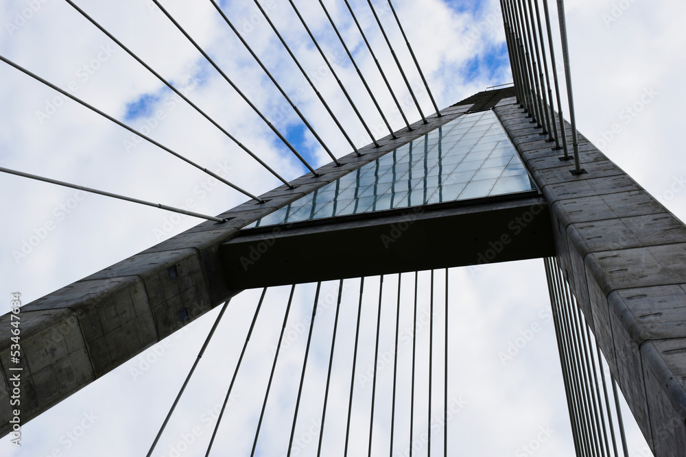 Fototapeta premium Suspension bridge concrete tower frame detail with heavy white steel tube cables. perspective view. blue summer sky beyond. construction and architecture concept. spiral welded steel pipe structure