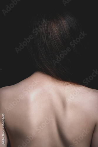 Beauty and fashion concept. Studio shot of beautiful wild looking woman with naked back standing in front of camera. Model with long brown hair and smooth skin. Toned image with brown color