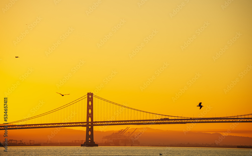 Obraz premium Oakland Bay Bridge landmark in San Francisco, transportation industry architecture photography during a beautiful sunrise with spectacular sky. Travel to California, United States.
