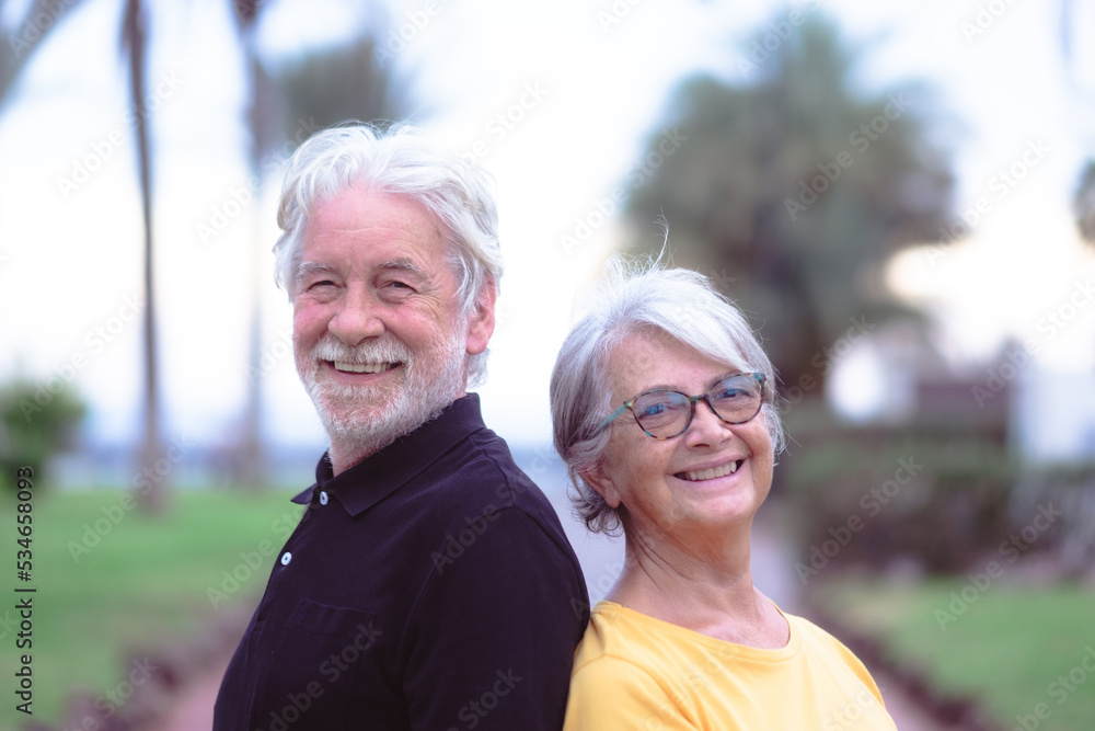 Portrait of happy lovely senior couple in outdoor public park at sunset. Two caucasian elderly people looking at camera smiling enjoying good time together
