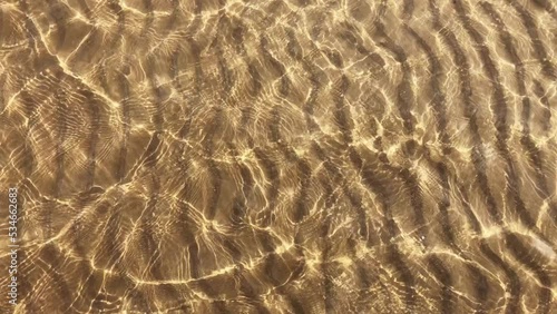 Transparent water ripples and gold sand with waves, sunlight glare. Sea floor pattern background.