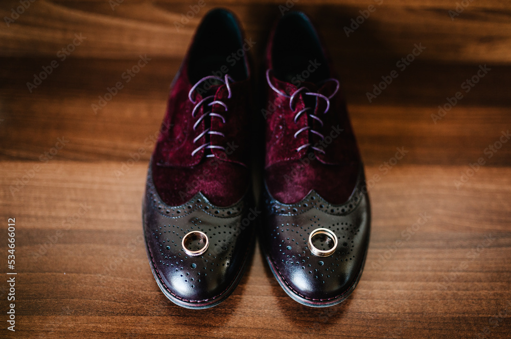 Two gold wedding rings on men's shoes on a wooden brown background. Wedding rings of the bride and groom. Engagement. Two gold wedding rings on men's shoes on a wooden brown background. Wedding rings of the bride and groom. Engagement.