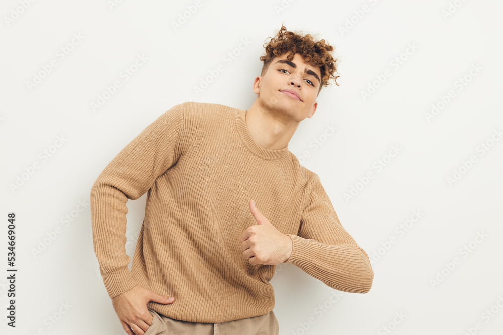 a cute, stylish, curly-haired man stands on a light background looking pleasantly into the camera with a slight smile on his face showing thumbs up a cute, stylish, curly-haired man stands on a light background looking pleasantly into the camera with a slight smile on his face showing thumbs up