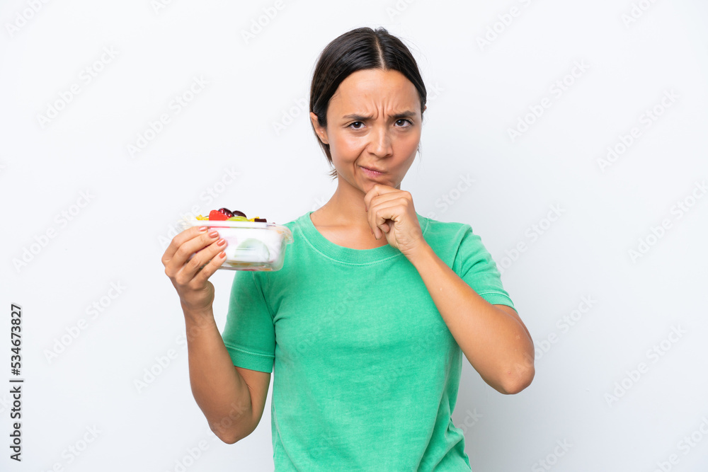 Young hispanic woman holding a bowl of fruit isolated on white background thinking Young hispanic woman holding a bowl of fruit isolated on white background thinking
