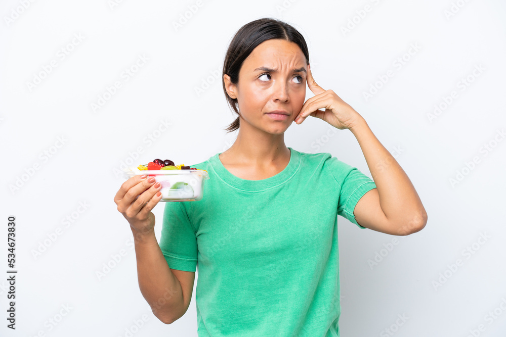 Young hispanic woman holding a bowl of fruit isolated on white background having doubts and thinking Young hispanic woman holding a bowl of fruit isolated on white background having doubts and thinking