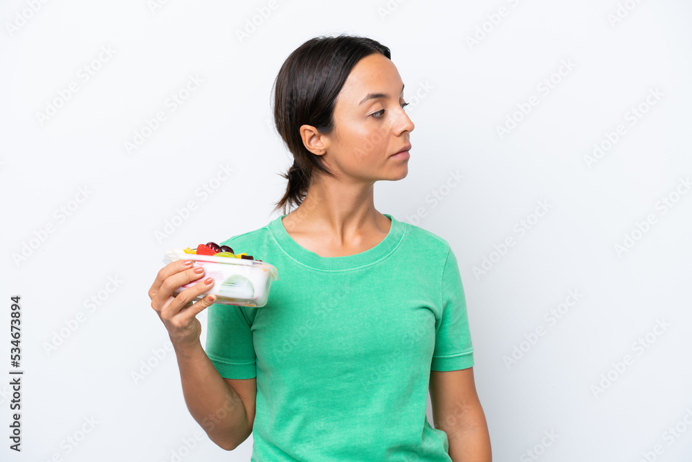 Young hispanic woman holding a bowl of fruit isolated on white background looking to the side Young hispanic woman holding a bowl of fruit isolated on white background looking to the side