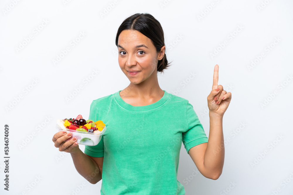Young hispanic woman holding a bowl of fruit isolated on white background showing and lifting a finger in sign of the best Young hispanic woman holding a bowl of fruit isolated on white background showing and lifting a finger in sign of the best
