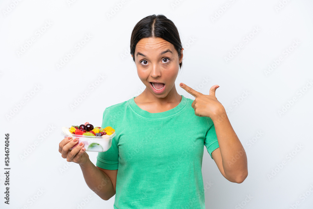 Young hispanic woman holding a bowl of fruit isolated on white background giving a thumbs up gesture Young hispanic woman holding a bowl of fruit isolated on white background giving a thumbs up gesture
