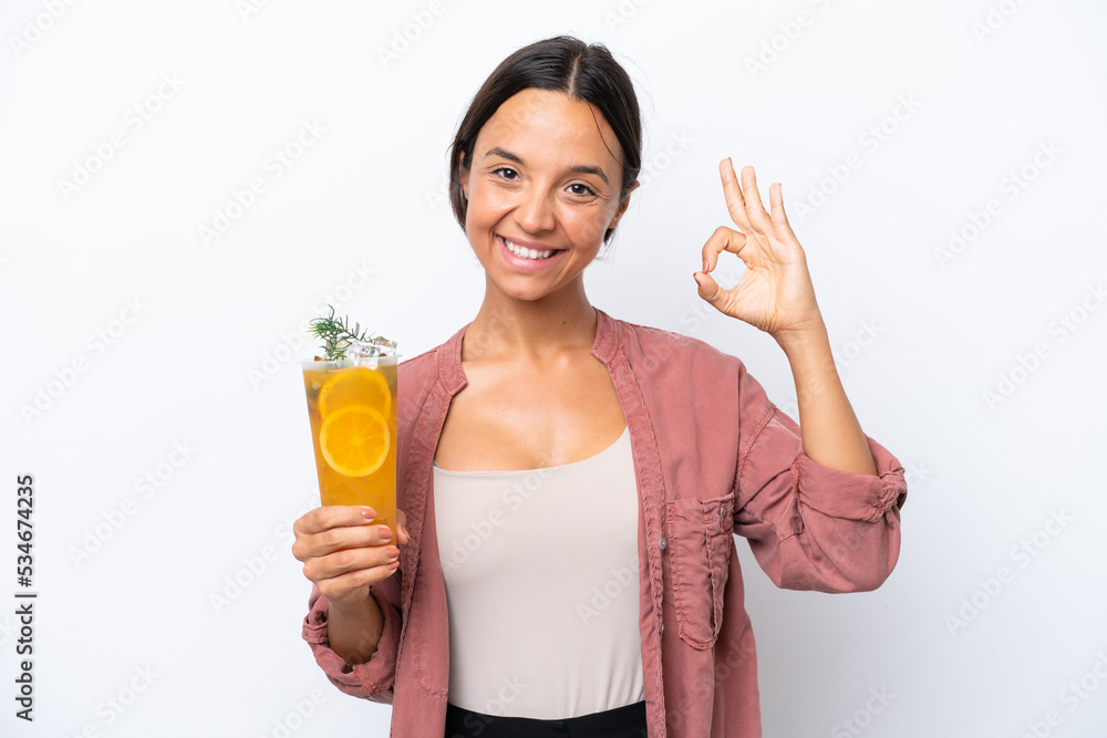 Young hispanic woman holding a cocktail isolated on white background showing ok sign with fingers Young hispanic woman holding a cocktail isolated on white background showing ok sign with fingers