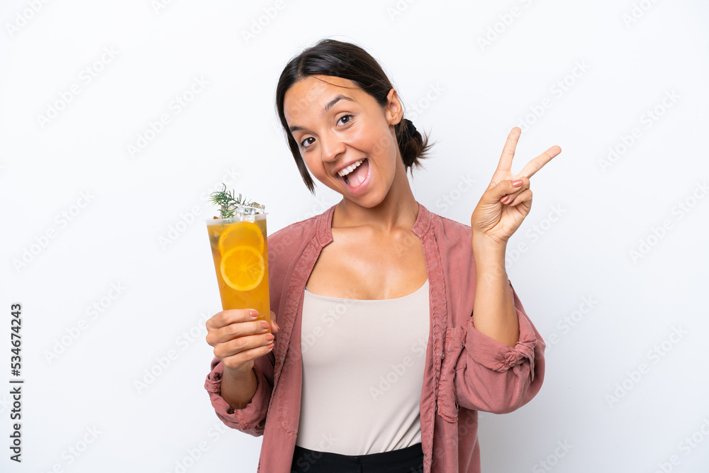 Young hispanic woman holding a cocktail isolated on white background smiling and showing victory sign Young hispanic woman holding a cocktail isolated on white background smiling and showing victory sign