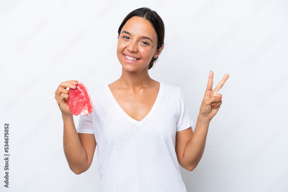 Young hispanic woman holding a piece of meat isolated on white background smiling and showing victory sign Young hispanic woman holding a piece of meat isolated on white background smiling and showing victory sign