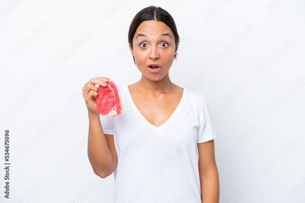 Young hispanic woman holding a piece of meat isolated on white background with surprise and shocked facial expression Young hispanic woman holding a piece of meat isolated on white background with surprise and shocked facial expression