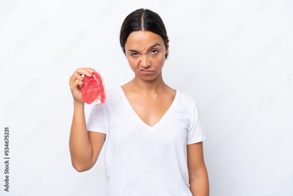Young hispanic woman holding a piece of meat isolated on white background with sad expression Young hispanic woman holding a piece of meat isolated on white background with sad expression