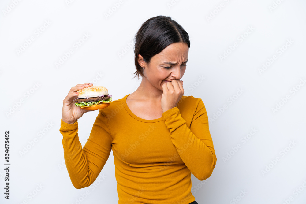 Young hispanic woman holding a burger isolated on white background having doubts Young hispanic woman holding a burger isolated on white background having doubts