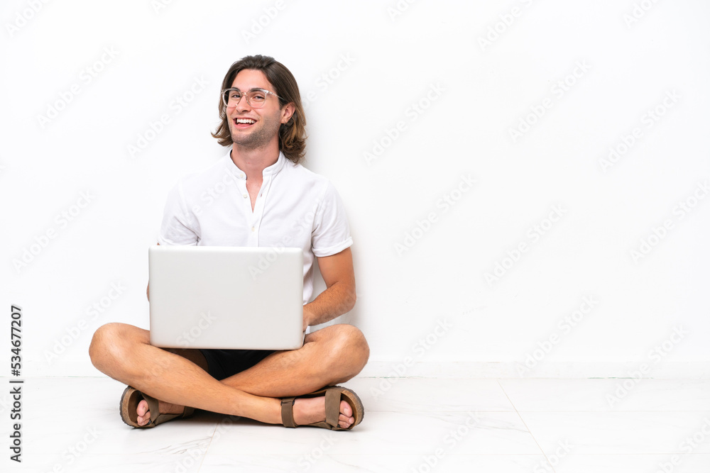 Young handsome man with a laptop sitting on the floor isolated on white background with arms crossed and happy Young handsome man with a laptop sitting on the floor isolated on white background with arms crossed and happy