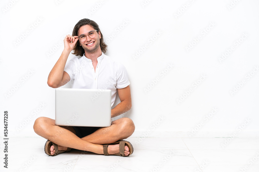 Young handsome man with a laptop sitting on the floor isolated on white background with glasses and happy Young handsome man with a laptop sitting on the floor isolated on white background with glasses and happy