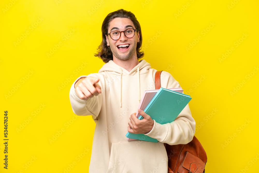 Young student handsome man isolated on yellow background surprised and pointing front Young student handsome man isolated on yellow background surprised and pointing front
